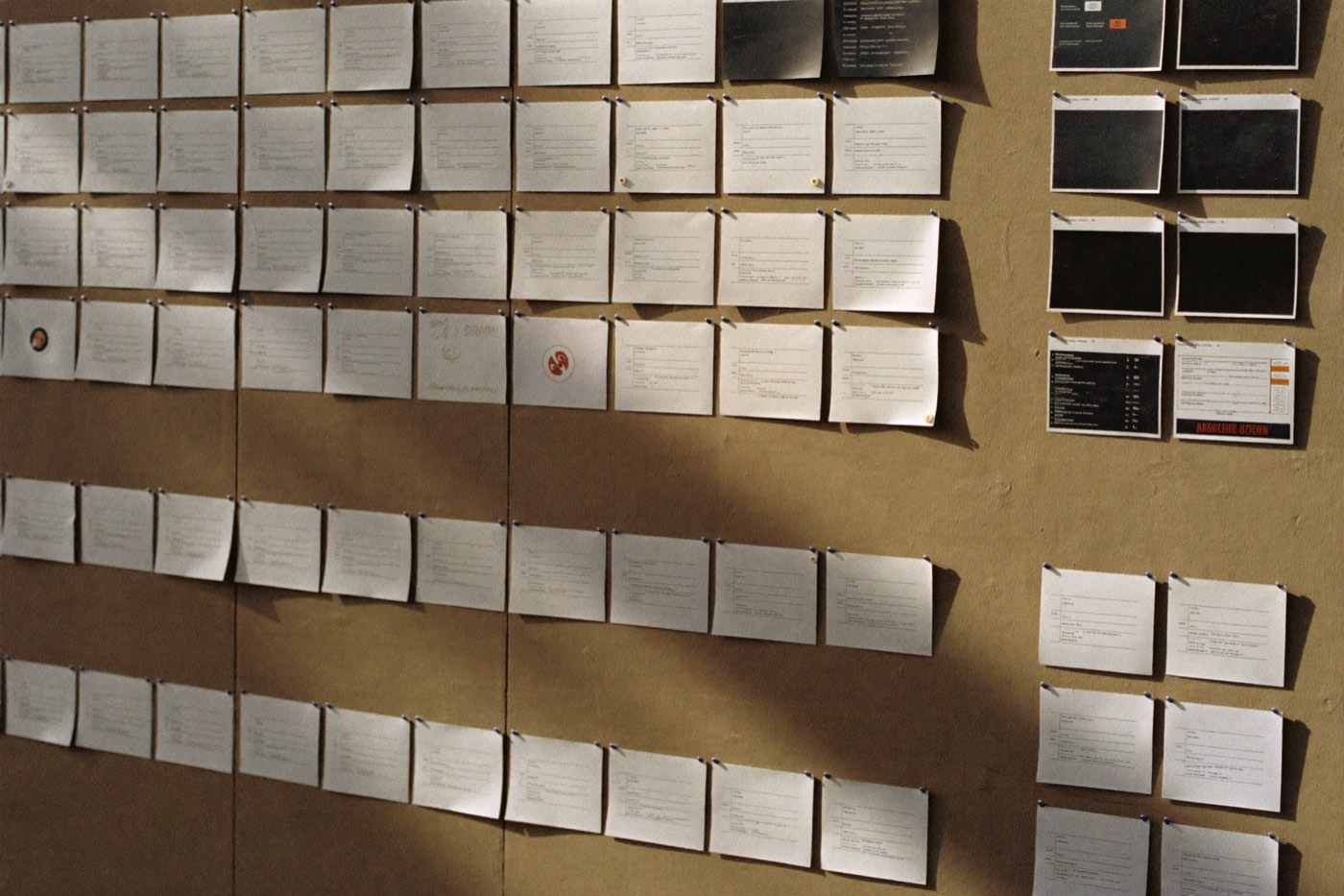 A bone plaster wall covered in pinned index cards and printed interface screens